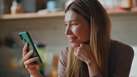 girl scrolling news feed smartphone at kitchen close up. smiling woman looking