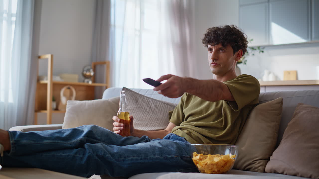 Keder sig mand skifter kanaler på tv med fjernbetjening ved sofaen tæt på