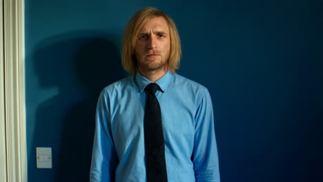 man with a concerned or disgusted expression standing against a blue wall