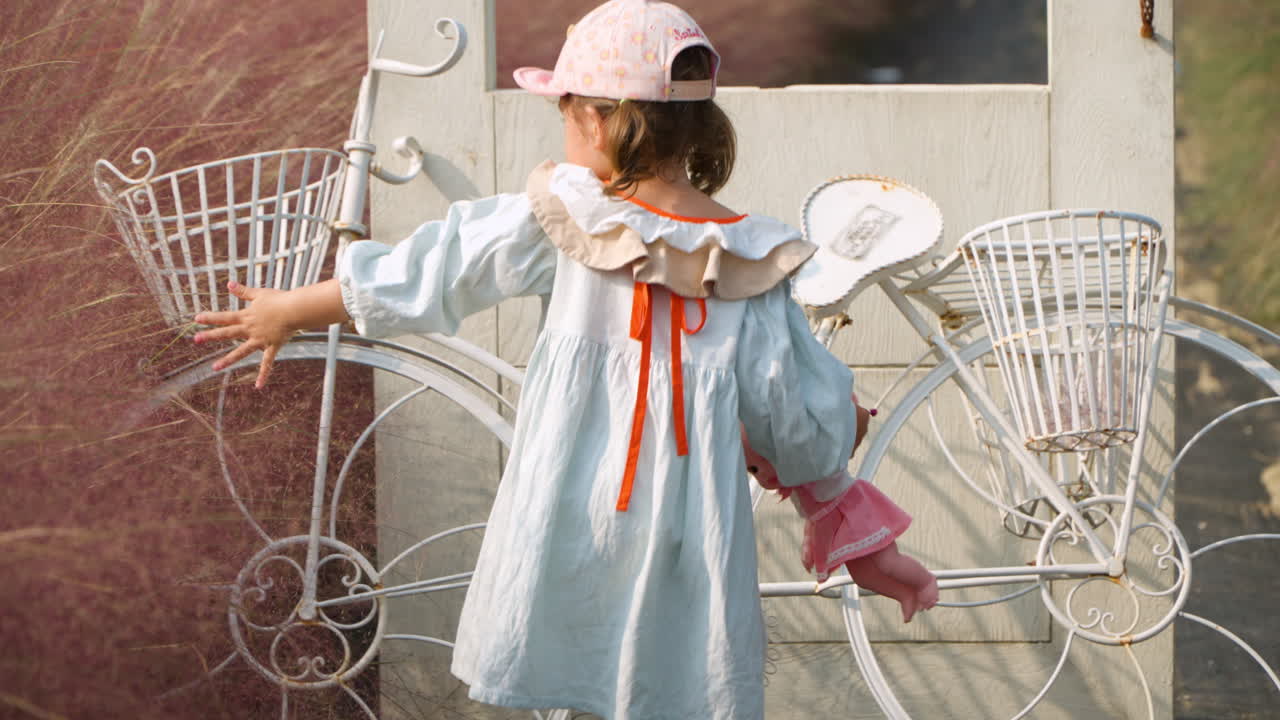 작은 소녀 유아는 포치온의 허브 아일랜드 공원에서 손으로 분홍색 무힐리 잔디를 만집니다.