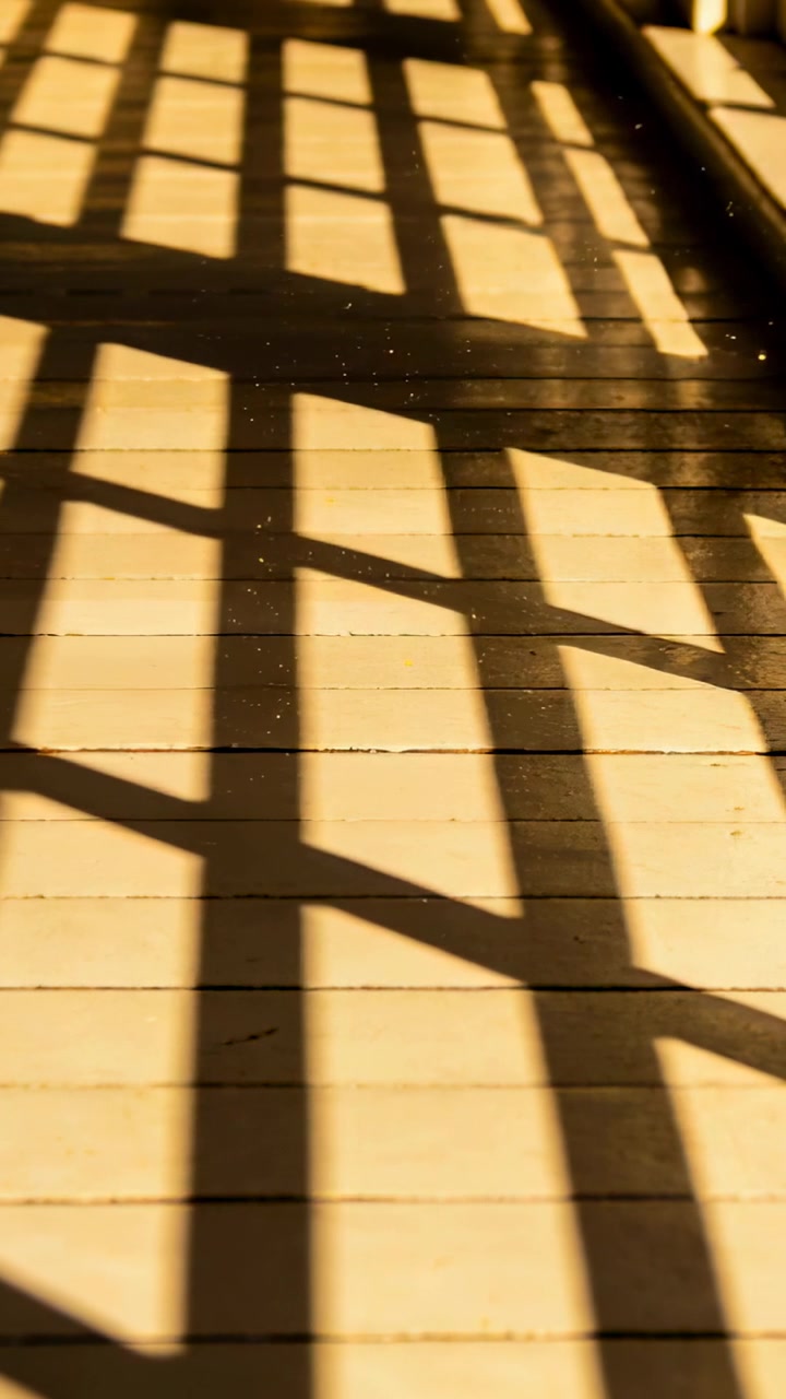 Vertical video: Shifting sunlight casting paned window shadows on plank floor in room with rail