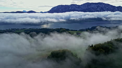 Wunderschöne-Luftdrohne,-Die-Am-Abend-über-Einem-Wald-Durch-Weiße-Wolken-Mit-Einer-Bergkette-Im-Hintergrund-Aufgenommen-Wurde