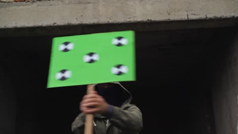 a man wearing a black face mask holds a poster in his hands and waves them in different directions. copy space tracking points. blank green screen board.