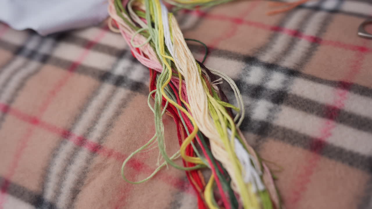 Haz de hilos de bordar de colores sobre una suave superficie de tela a cuadros, que muestra la textura vibrante y el detalle de los tonos de hilo utilizados para labores de aguja, costura y preparación de arte creativo hecho a mano.