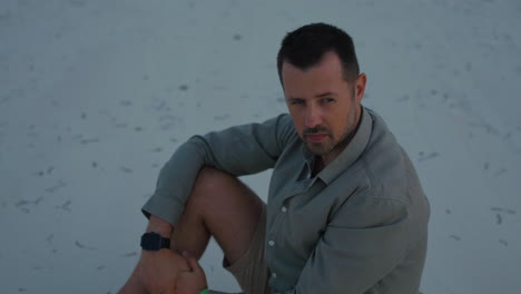 lonely and sad man sits on white sand beach in silence, thinking about life, during twilight