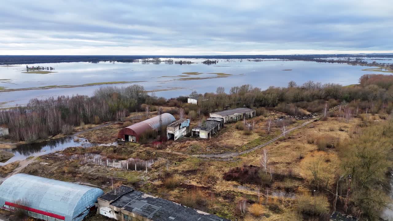 구름 은 회색 하늘을 반영하는 물로 인 잔디로 된 홍수 평야와 함께 오래된 버려진 창고의 공중 도리