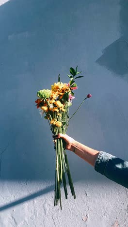 hand holding a colorful bouquet of flowers against a wall