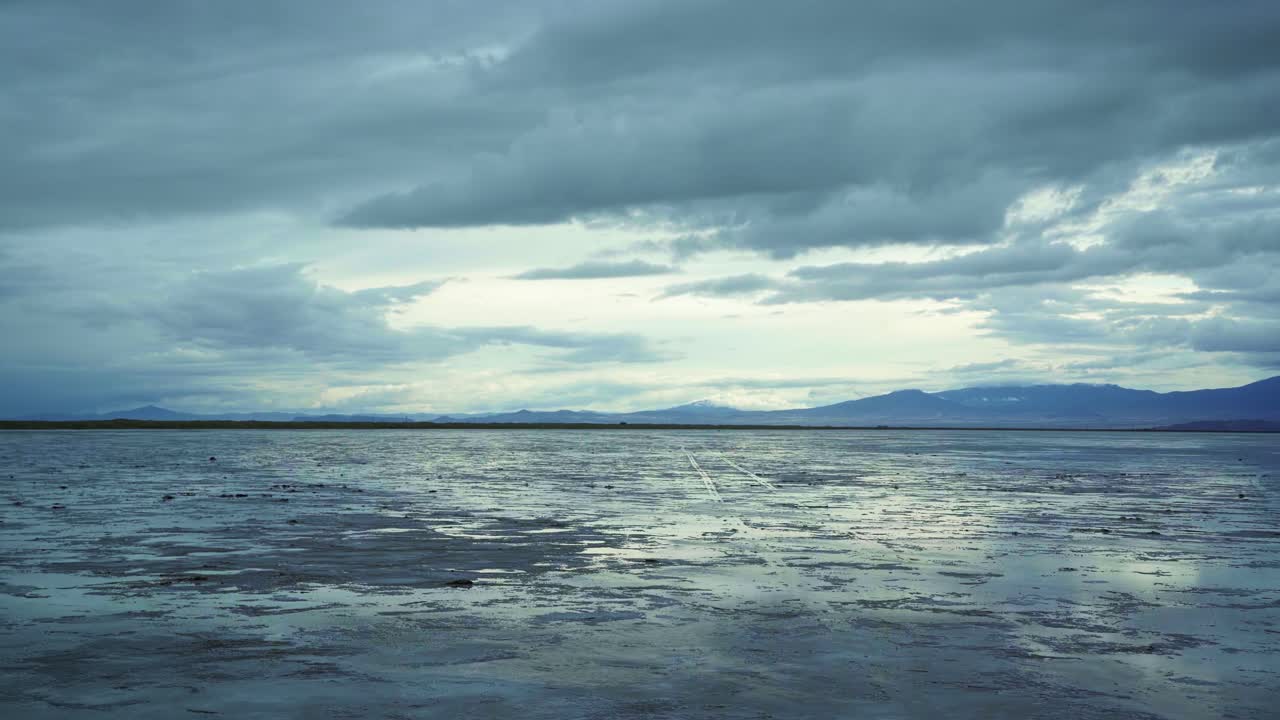Wide landscape tilting up shot of the beautiful Bonneville Salt Flats in Utah near Wendover, Nevada on a stormy spring evening with patches of dry and wet spots and mountains in the background