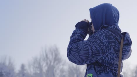 garçon dans une veste bleue et un capuchon tenant les jumelles jusqu'à leurs yeux dans un paysage enneigé