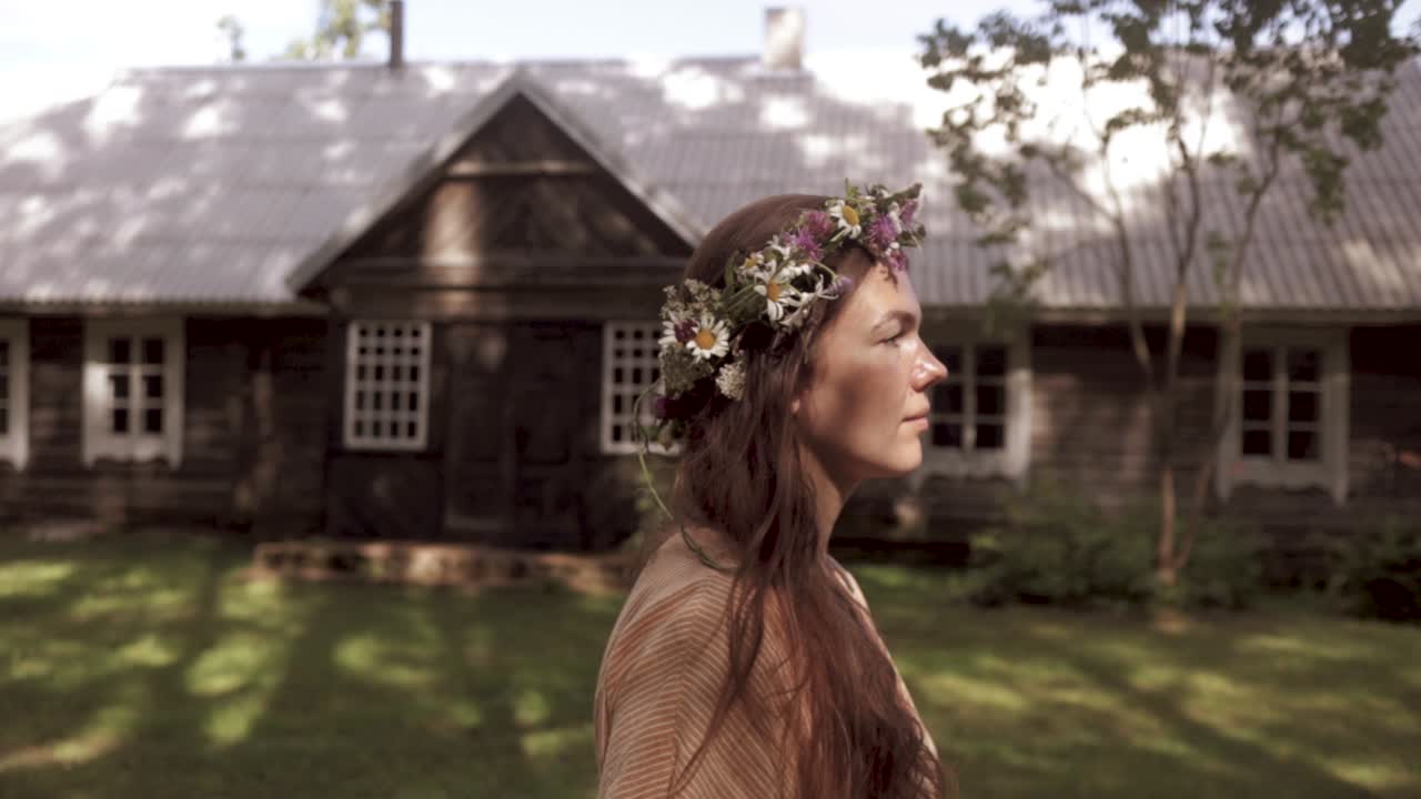 una mujer con la corona de flores camina por una antigua casa de campo mientras la cámara la sigue, con clasificación de color, cámara lenta