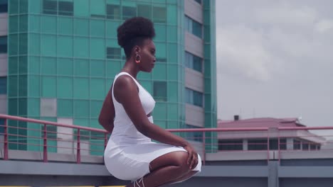 A-black-girl-in-a-white-dress-stands-on-a-rooftop,-gazing-over-the-city