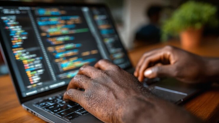 Focused Programming Session: A Close-Up of Hands Typing Code on a Laptop with Colorful Display in a Welcoming Environment