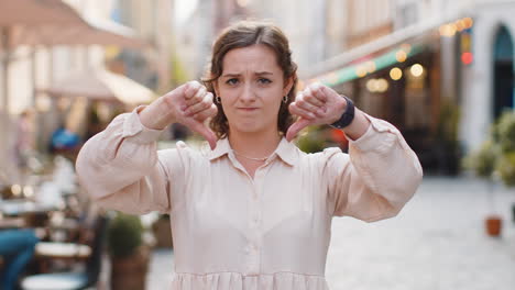 upset young woman showing thumbs down sign, disapproval, dissatisfied bad work, mistake in city