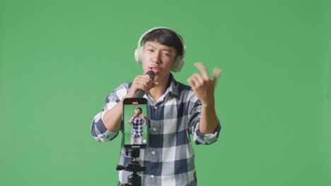 smartphone record young asian teen boy holding a microphone and rapping on the the green screen background