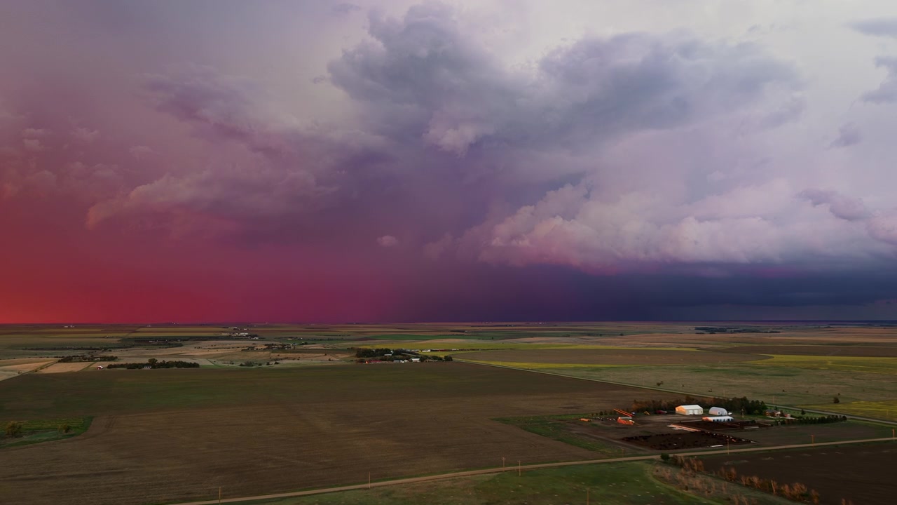 Varma solnedgångsfärger fyller en stormig himmel när blixtar slår ner över åkermark, flygfoto med drönare i 4k.