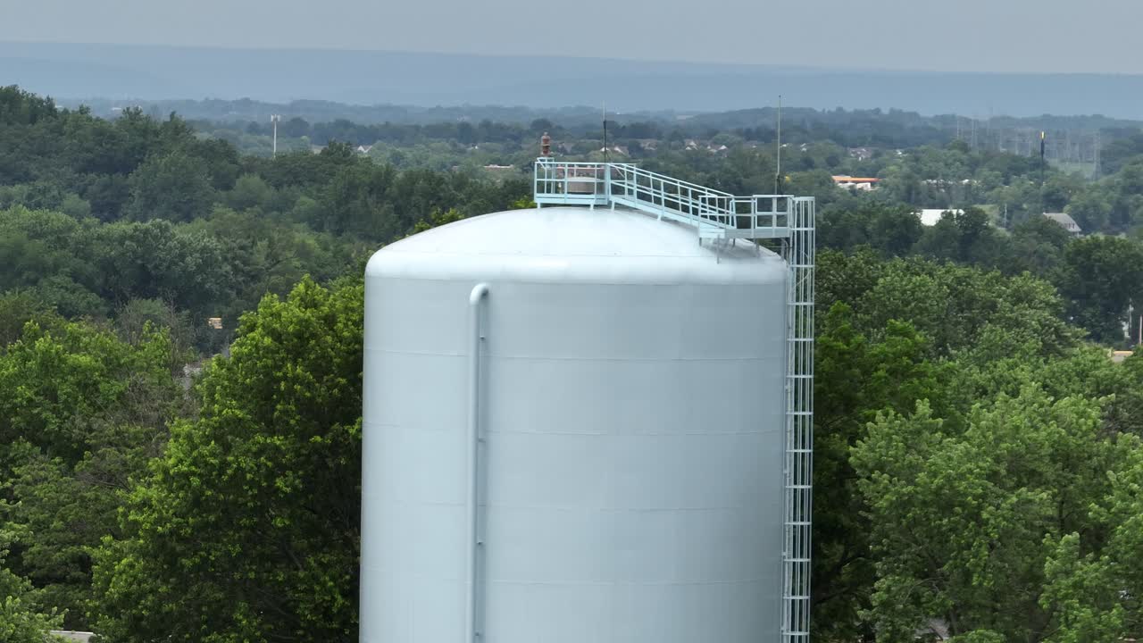 Water tower above lush green trees in small-town of America and hills. Aerial view of rural infrastructure in the United States. Utility tower in United States