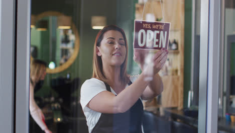 female hairdresser changing sign board from closed to open at hair salon