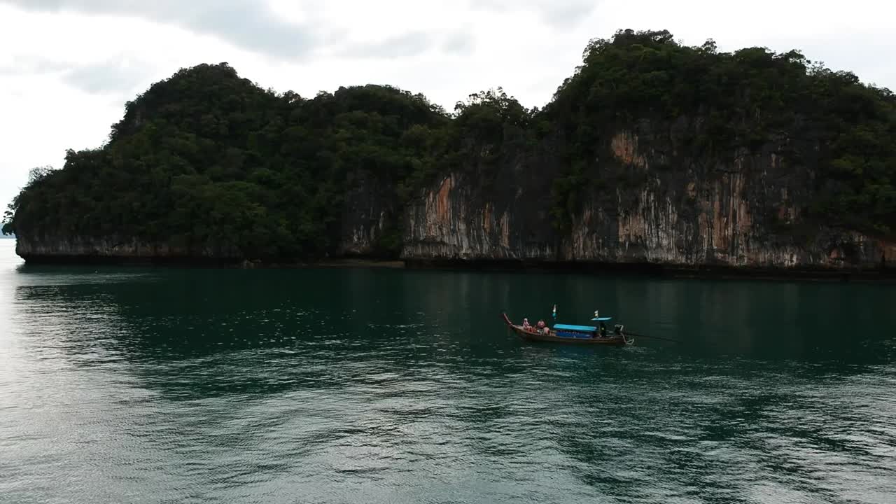 Riprese con drone di una barca longtail che naviga intorno alle isole di Krabi, Thailandia, con formazioni rocciose calcaree che spuntano dall'acqua e l'oceano sullo sfondo