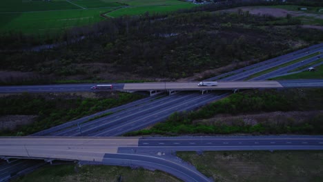 Aerial-perspective-of-a-major-interstate-crossroads-showing-semi-trucks-and-cars-navigating-through-at-dusk,-highlighting-rural-Pennsylvania’s-infrastructure