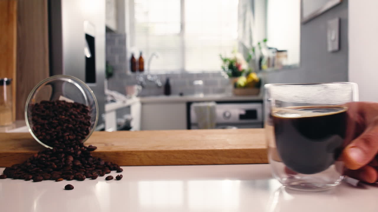 Unas manos colocan una taza de café caliente en la encimera de la cocina con granos de café