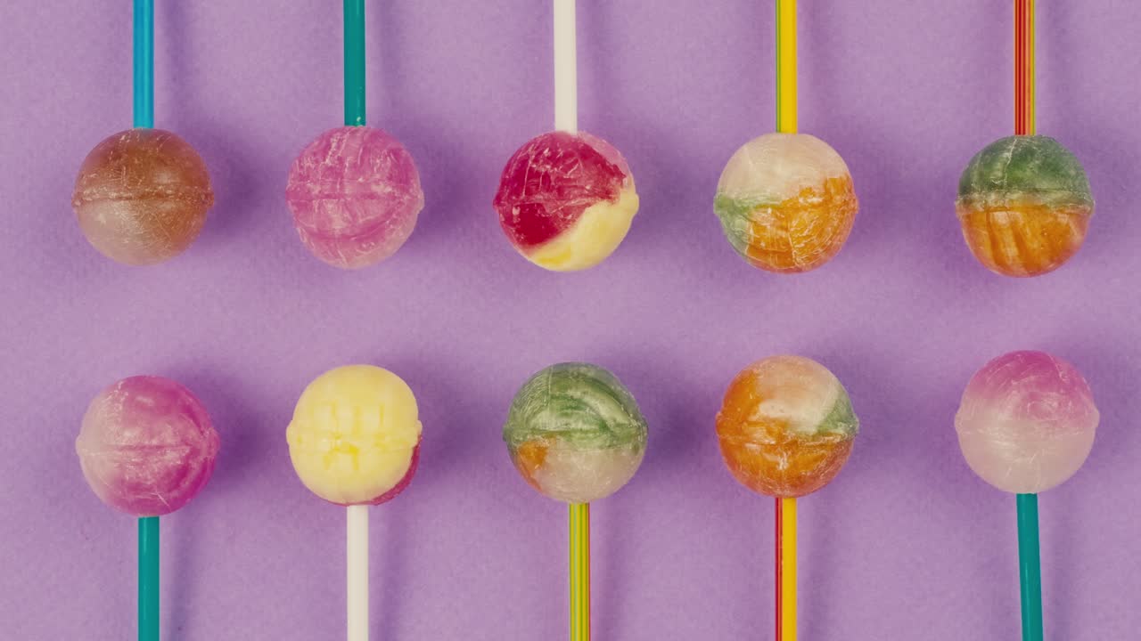 Sweet lollipops with glitter sprinkles on color purple background zoom frame. Bright texture sugar candies close up top view. Composition of favorite children's summer sweets. Studio shot for shop, supermarket, confectionery
