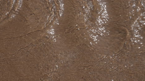 sand being moved by the tide as ripples of water recede from the sea