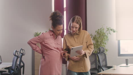 two pregnant woman looking at tablet and talking in the office