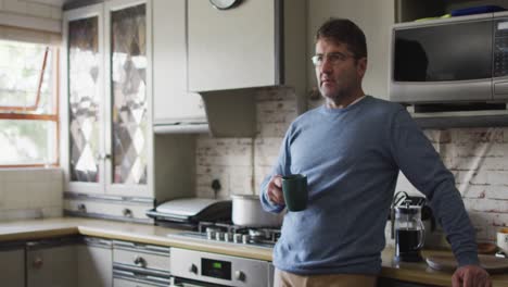 Thoughtful-caucasian-man-drinking-coffee-in-kitchen-at-home