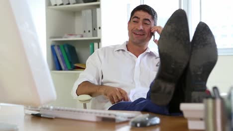 Businessman-answering-the-phone-with-feet-up-on-desk