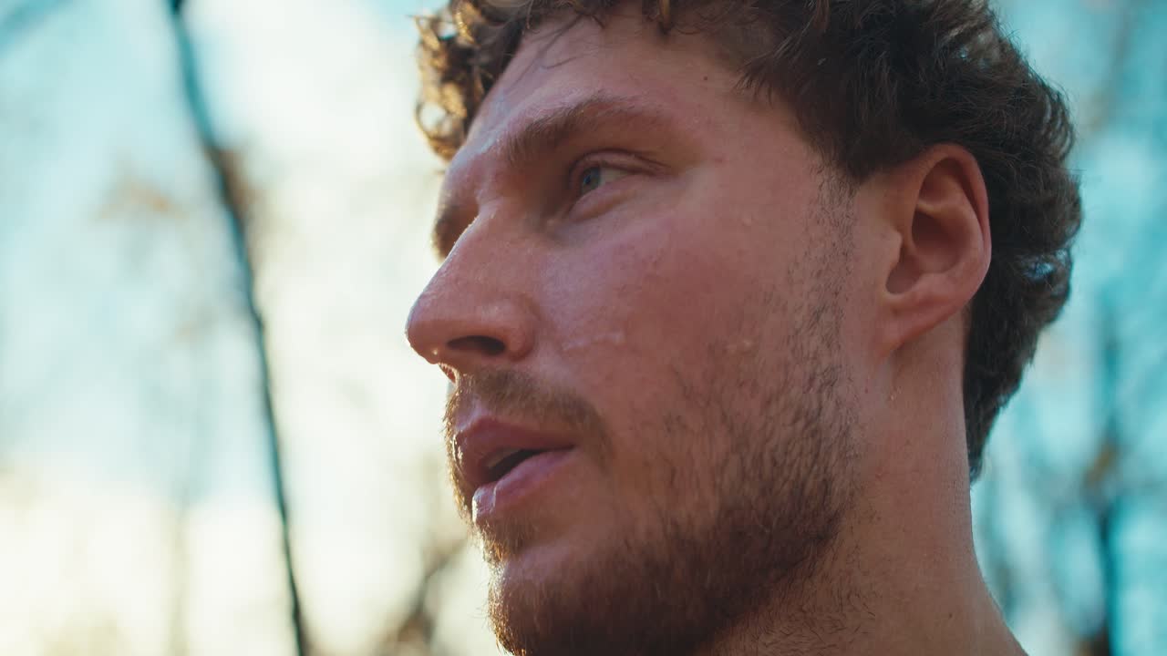 un hombre tranquilo y cansado con el cabello rizado y la barba limpia el sudor de su cara después de un duro trote por la mañana en otoño. fotografía en primer plano de un atleta masculino descansando después de una carrera y limpiando el sudor del rostro