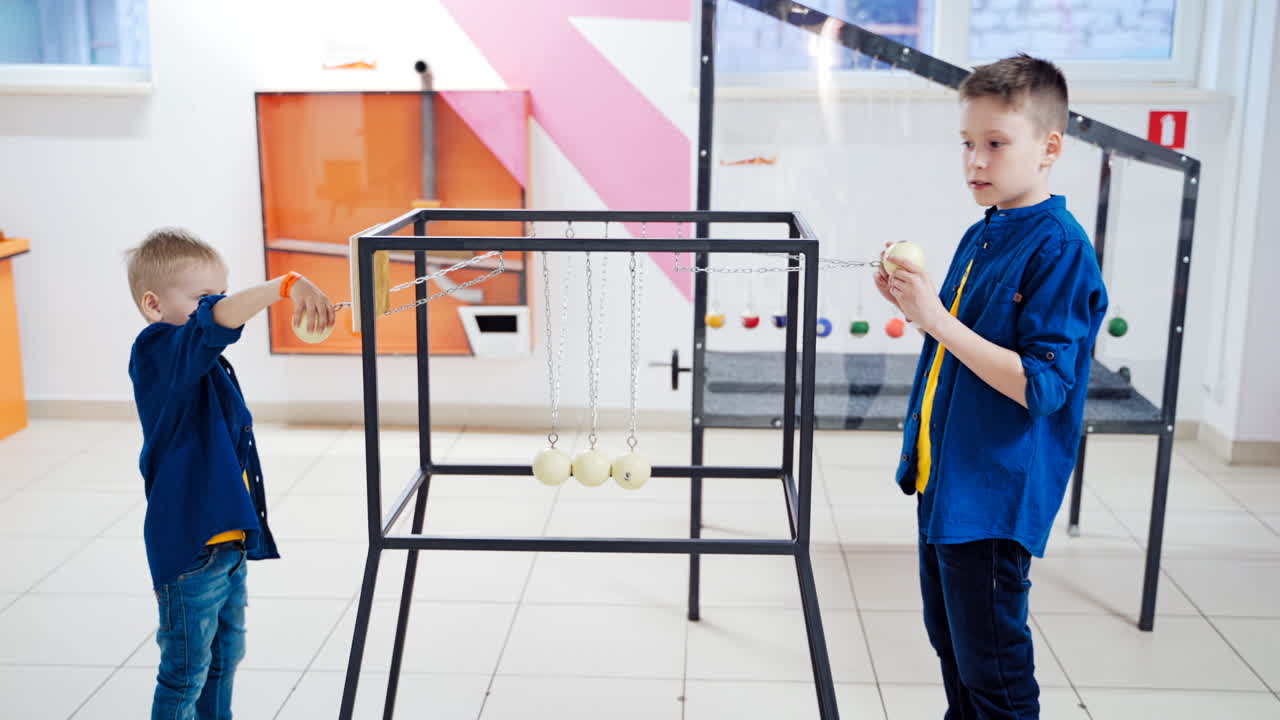 Newton's cradle. Action and reaction concept. Series of swinging spheres. Kids are playing.