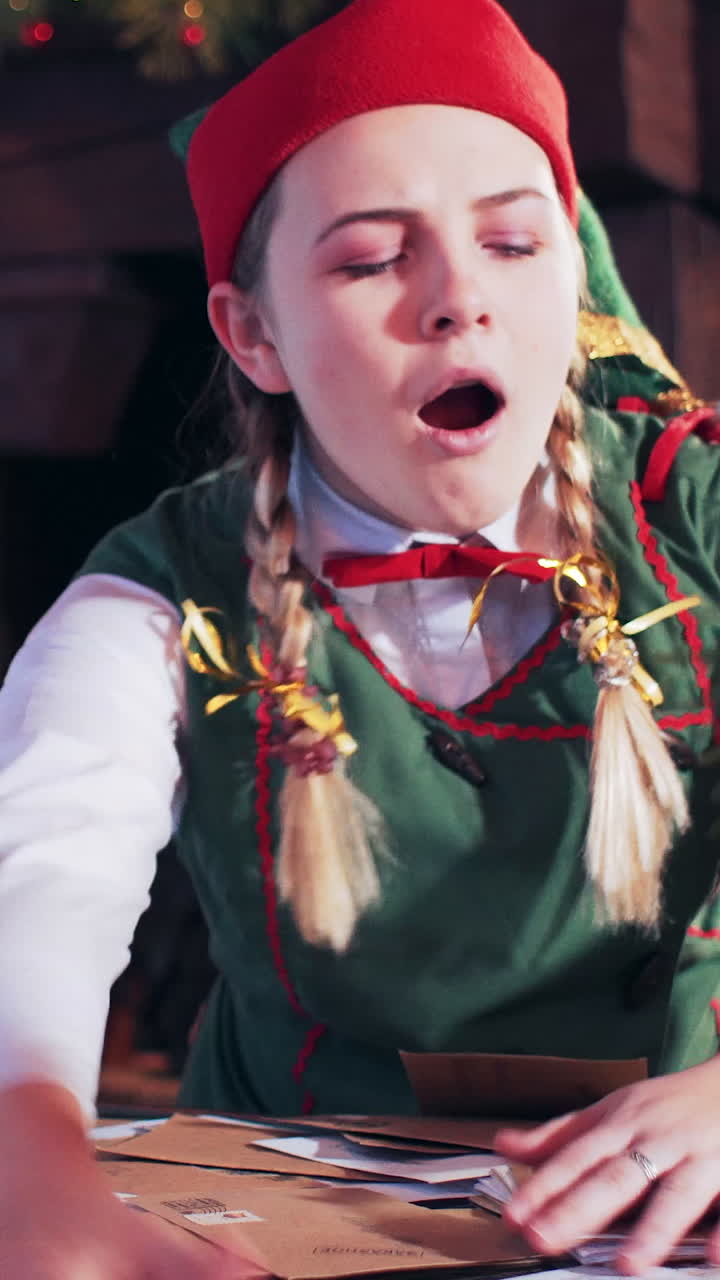 The girl falls asleep sitting at a table with letters in a room with New Year's decorations and a Christmas tree. Vertical video