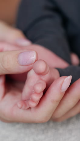 female hand with brown wrist watch strokes tiny baby toes. cute infant's feet in mother's hands. close up. vertical video