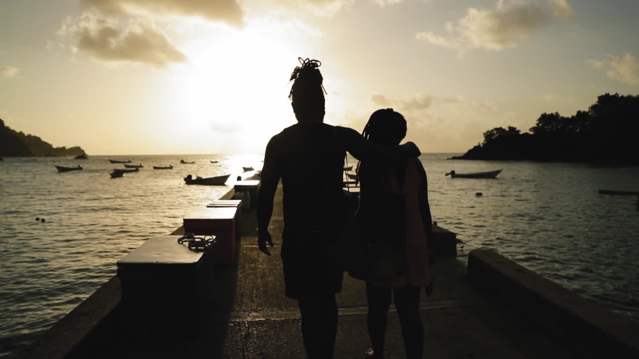 Middle aged couple in love walking down a dock holding hands with boats surrounding them in Tobago