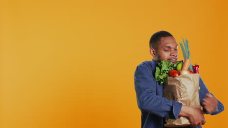 joven luchando para llevar una bolsa de papel llena de frutas y verduras biológicas frescas