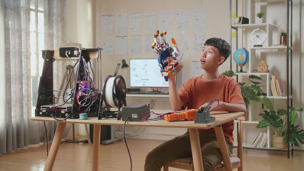 3d 프린터를 가진 아시아 소년이 집에서 사이보그 손을 확인합니다.
