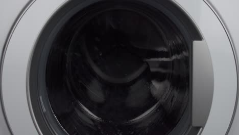 close up static shot of washing machine washing dark clothes