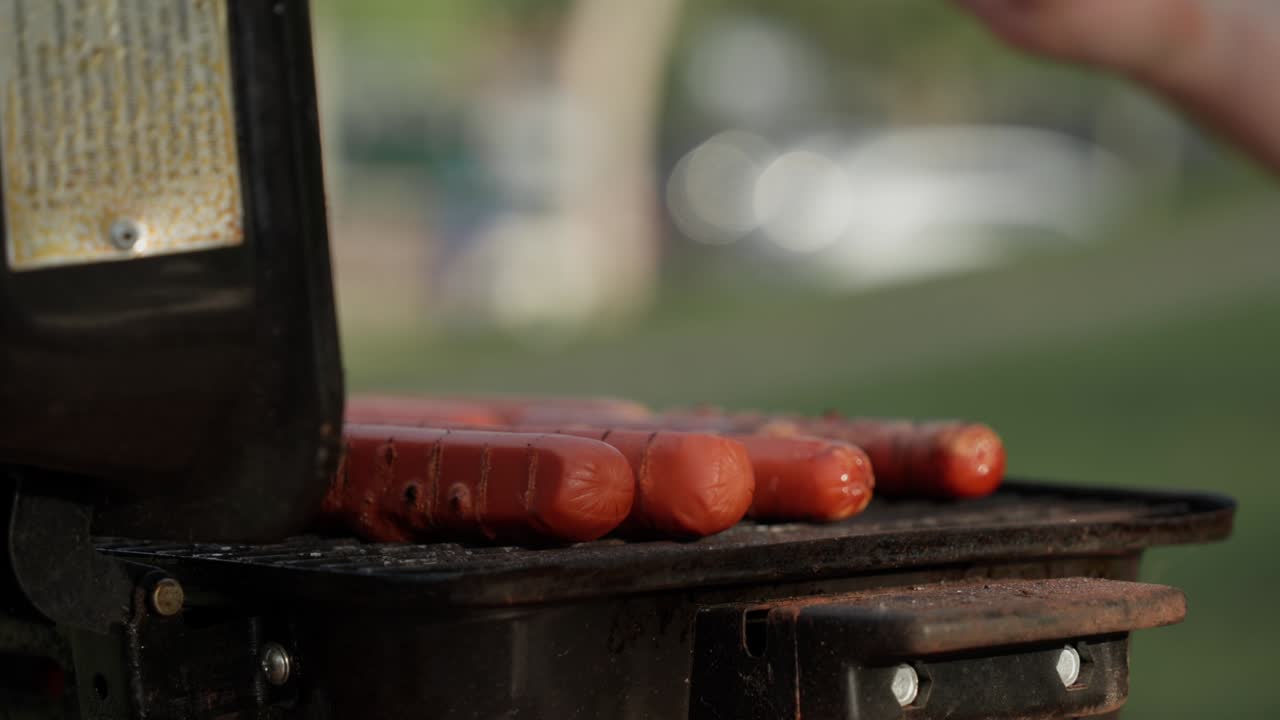 Close-up of sausages grilling on a barbecue, with a person blurred in the background