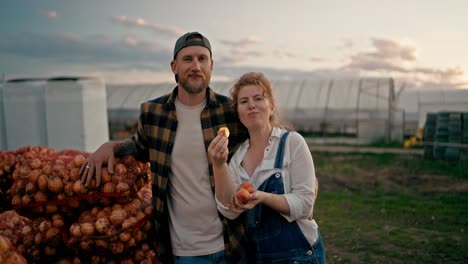 portrait of a happy farmer guy with his girlfriend eating peaches near bags of onions after a successful harvest season on the farm