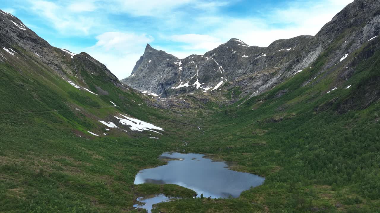 En fredfyldt dal med frodigt grønt og en sø omgivet af majestætiske bjerge i Norge