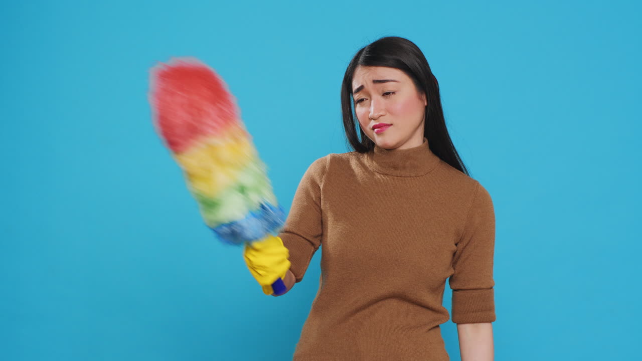 Tired professional maid cleaning furniture dust using colorful duster during cleaning session