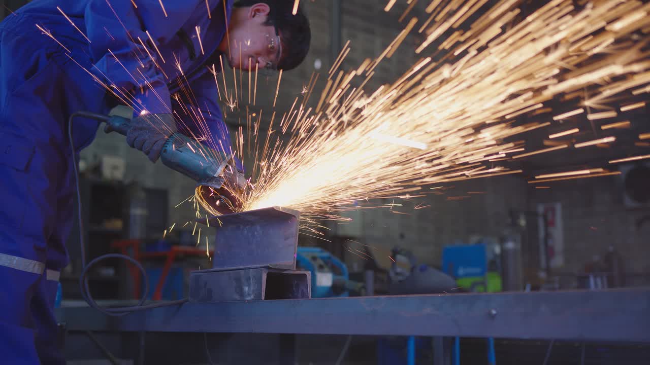 안전한 유니폼을 입은 아시아 남성 기술자 노동자 가죽, 전기 바, 공장 워크에서 강철 구조물에 는, 차고에서, 오렌지 보케 스파크가 으로 날아갑니다.