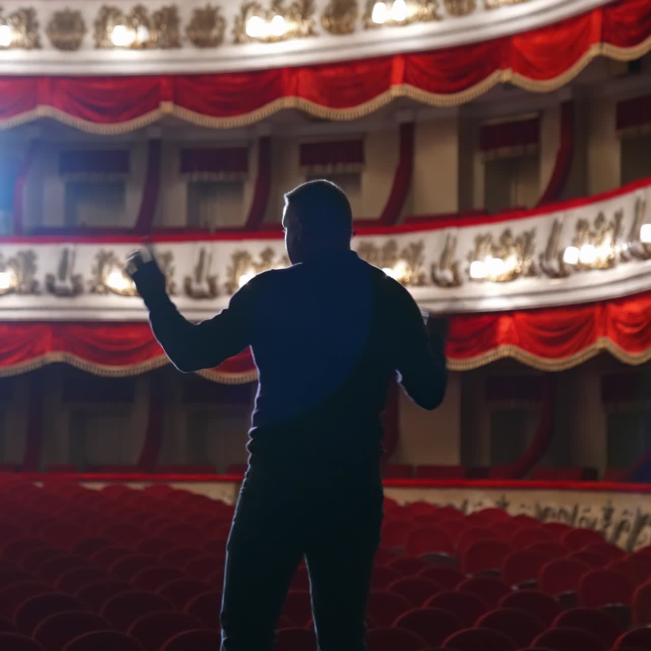 Announcer on a stage in theater. Bright round light on one person. Man in black suit performs to the auditorium. View from the back