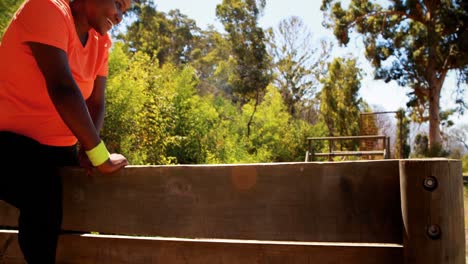 Trainer-assisting-woman-in-wooden-wall-climbing-during-obstacle-course