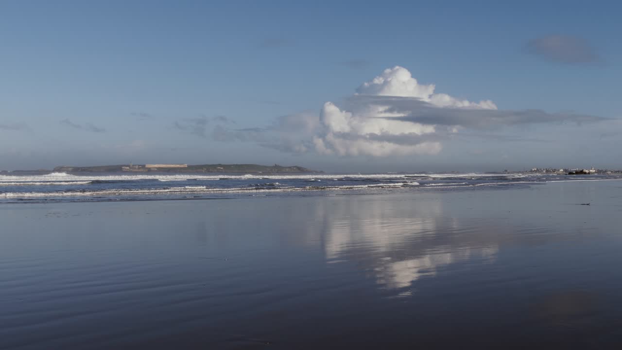 playa con nubes y reflejos, con el horizonte de la ciudad de essaouira, ciudad costera de pescadores.