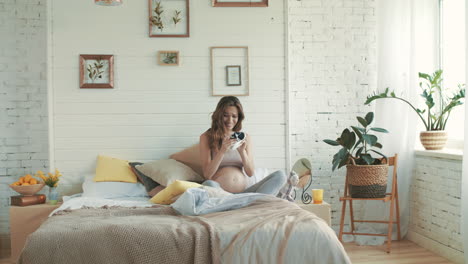 Madre-Del-Vientre-Sosteniendo-Camisa-De-Bebé-En-Casa.-Feliz-Mujer-Embarazada-Sentada-En-El-Dormitorio.