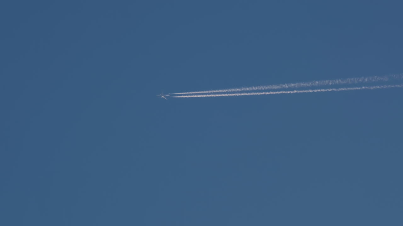 A passenger airplane with contrail against blue sky.