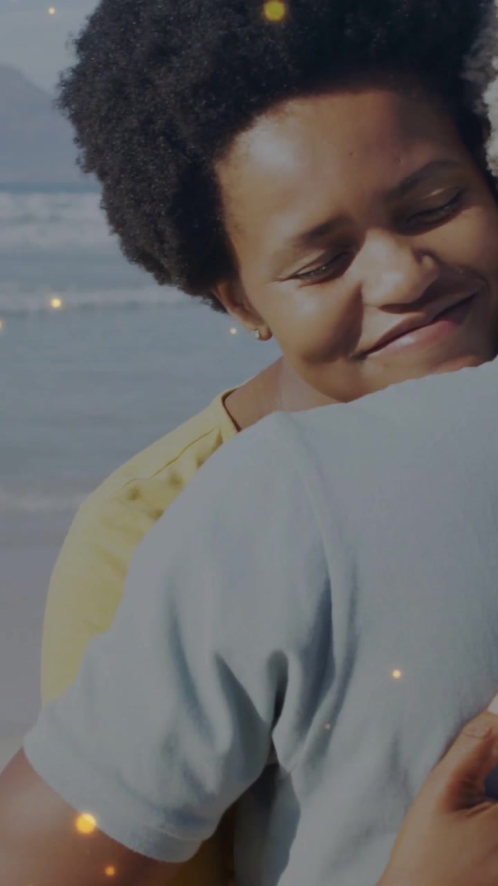 Vertical video: Woman leaning in seeking hug, couple hugging as golden glow floating above beach