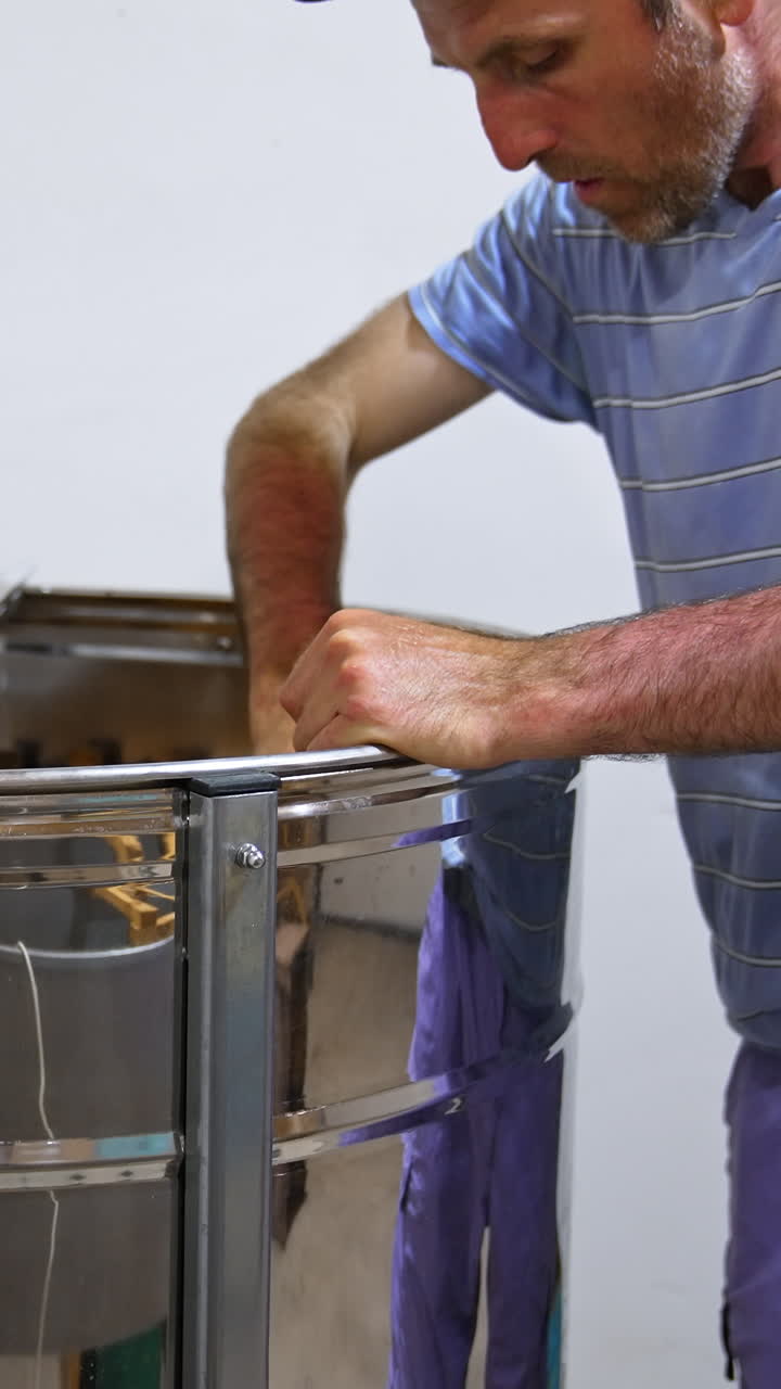 Bee farmer puts the frames into a metal barrel to get honey. Man carefully places the honeycombs into special apparatus. Vertical video