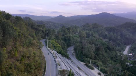 Aerial-view-of-lone-motorcyclist-crossing-Mae-Hong-Loop-road-at-sunset